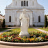 Monumental Sacred Heart of Jesus Marble Statue in front of a white building with a garden of flowers and plants.