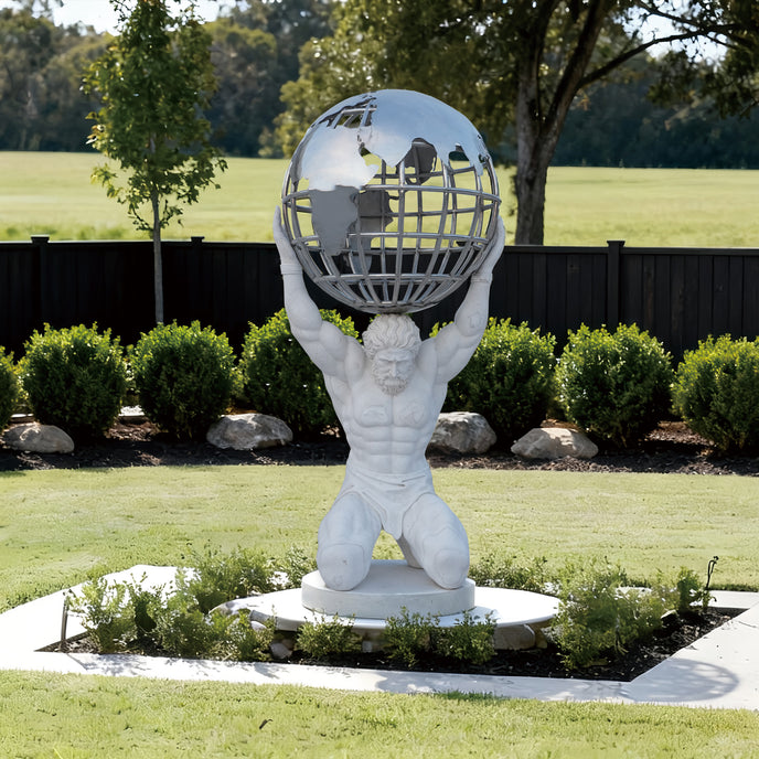 Majestic Atlas Holding Globe Marble Statue in an outdoor setting with greenery and a fence.