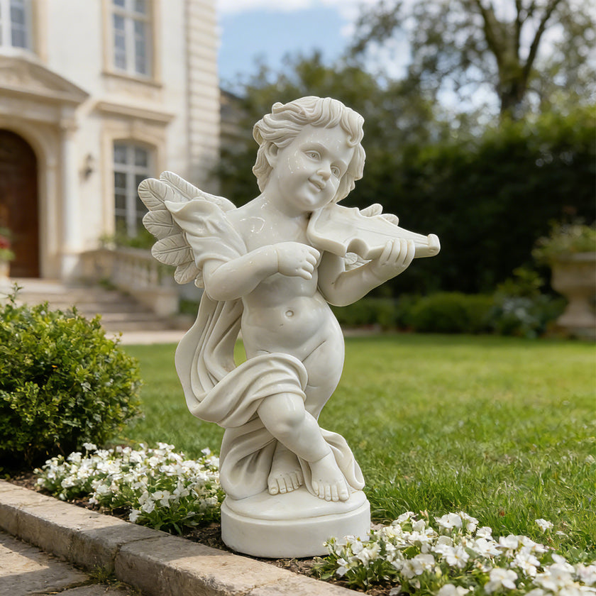 White marble cherub angel violin statue displayed in a luxury garden with flowers, lawn, and villa background.