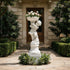 White marble cherub planter statue filled with flowers, displayed at a luxury villa entrance with hedges and classic garden pathway.