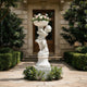 White marble cherub planter statue filled with flowers, displayed at a luxury villa entrance with hedges and classic garden pathway.