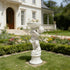 Natural white marble cherub flower planter statue placed in a villa garden with lawn, colorful flowers, and elegant home background.