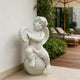 White marble cherub tambourine statue placed on a patio beside lounge chairs, greenery, and elegant outdoor home decor.