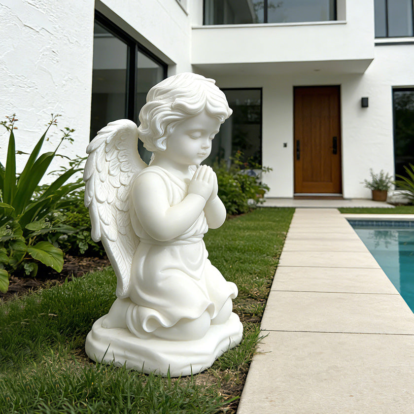 White marble praying angel statue displayed beside a modern pool garden, with folded hands, soft wings, and peaceful kneeling pose.