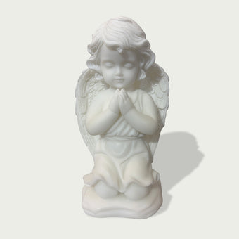 Close view of natural white marble praying angel figure with gentle face, folded hands, soft curls, and layered feather wings.