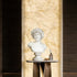 White marble male bust displayed on an indoor console table, adding classical sculpture charm to a luxury interior with warm marble wall lighting.