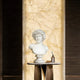 White marble male bust displayed on an indoor console table, adding classical sculpture charm to a luxury interior with warm marble wall lighting.