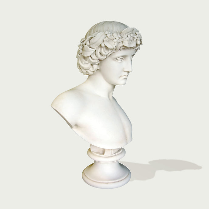 Natural white marble bust sculpture showing a young male figure with detailed flower crown, calm expression, and elegant museum-style form.