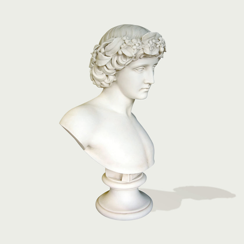 Natural white marble bust sculpture showing a young male figure with detailed flower crown, calm expression, and elegant museum-style form.