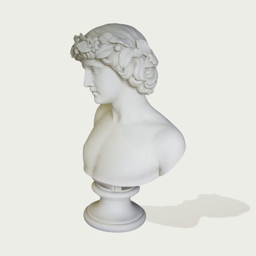 Side view of white marble male bust statue with laurel-style floral crown, soft carved hair, and classical profile on a clean background.