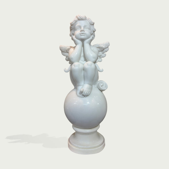 A white marble-style cherub statue with wings, seated on a round pedestal base against a light gray background.