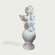 A white marble-style decorative sculpture of a seated cherub or angel with wings, resting on a round pedestal against a light gray background.