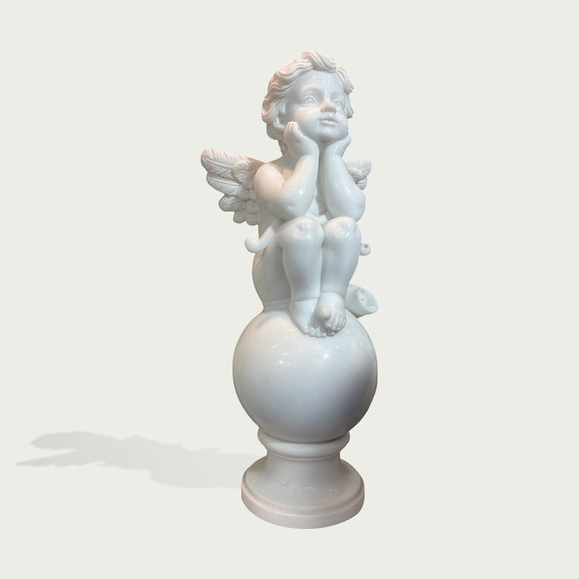 A white marble-style decorative sculpture of a seated cherub or angel with wings, resting on a round pedestal against a light gray background.