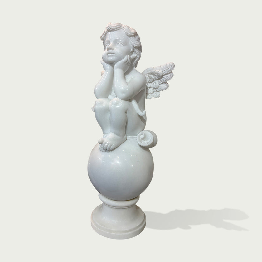 A white classical-style cherub statue seated on a round pedestal, photographed against a plain light gray background with a soft shadow.