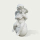 A white marble-style sculpture of a cherub or cupid sitting on a round base, holding a small flute, shown against a plain light gray background.
