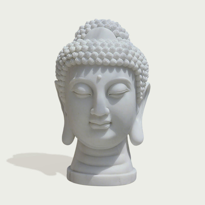 A white Buddha head bust sculpture with closed eyes and detailed hair curls, shown on a light beige background with a soft shadow.
