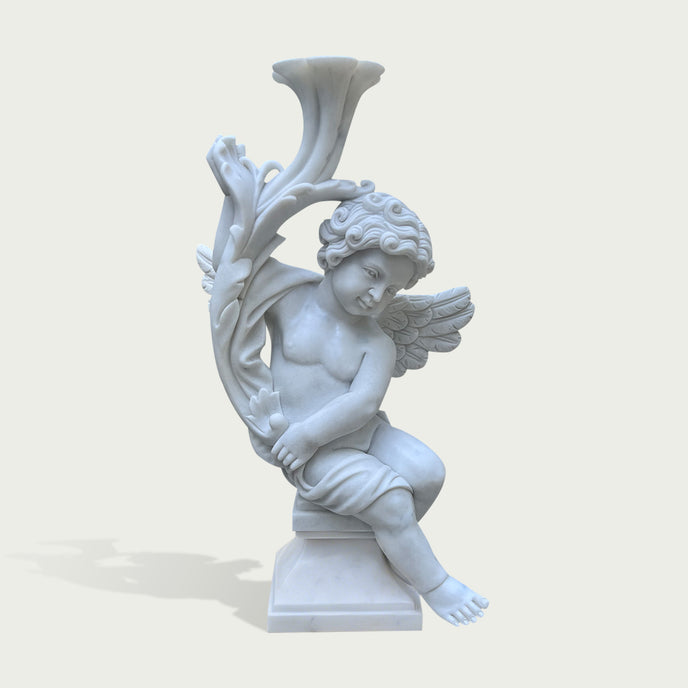 A white marble-style cherub statue seated on a pedestal, holding a large trumpet or horn-like vessel overhead, shown against a plain light beige background.