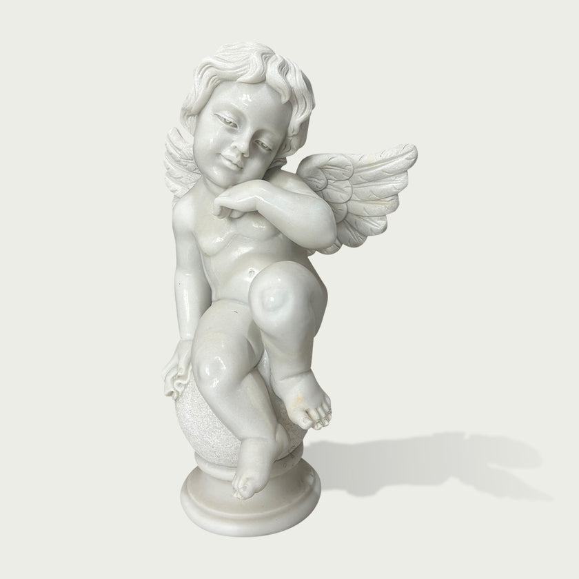 White marble cherub angel statue sitting on a decorative sphere with carved wings and detailed classical sculpture design