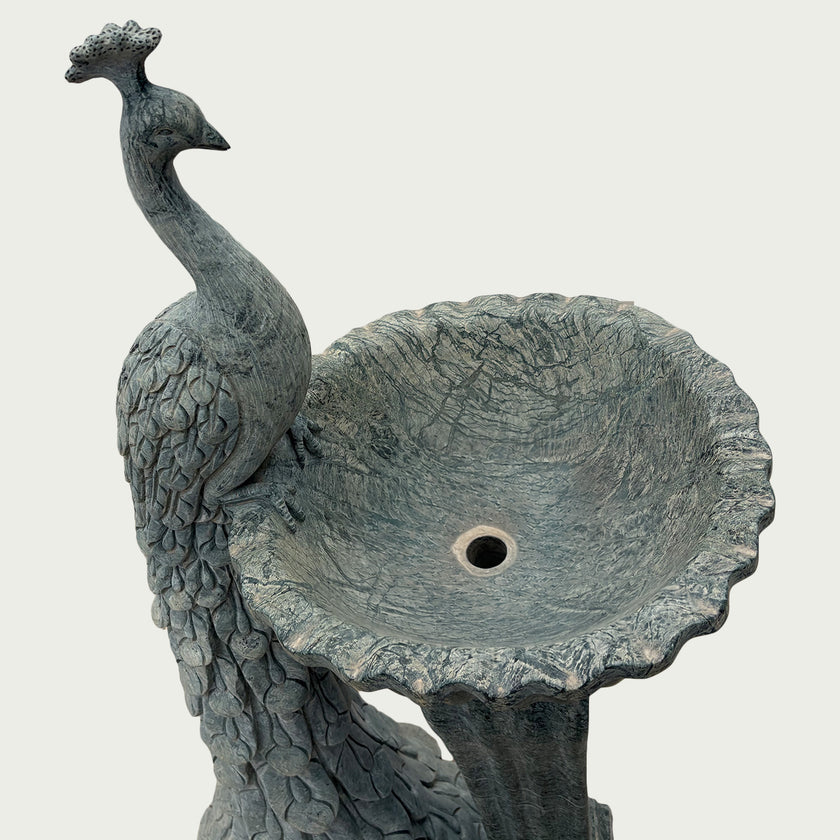 Close-up of antique grey marble peacock birdbath fountain with textured feathers and handcrafted outdoor sculpture details