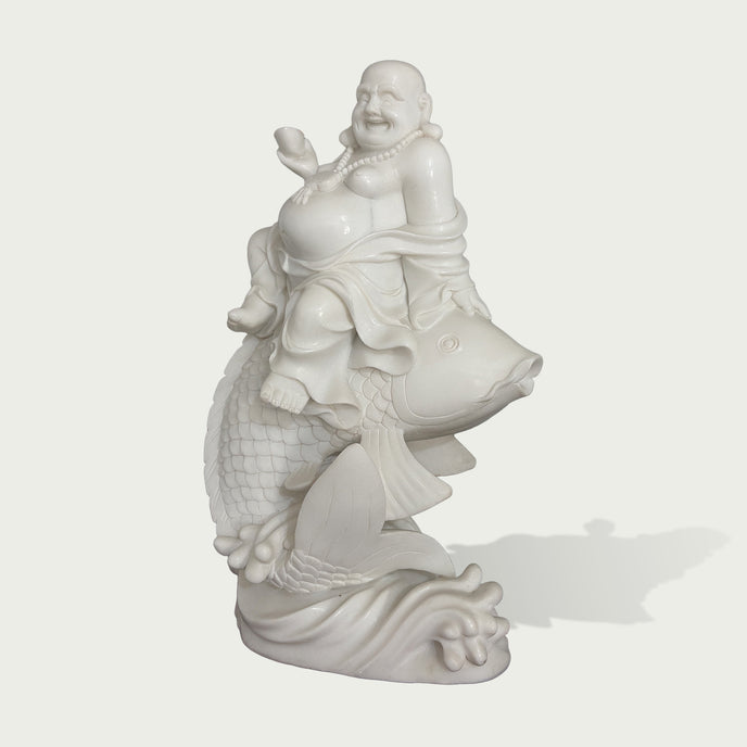 Three-quarter view of a white marble Buddha riding a fish statue, showing intricate carving, joyful expression, and traditional symbolism of wealth and prosperity.