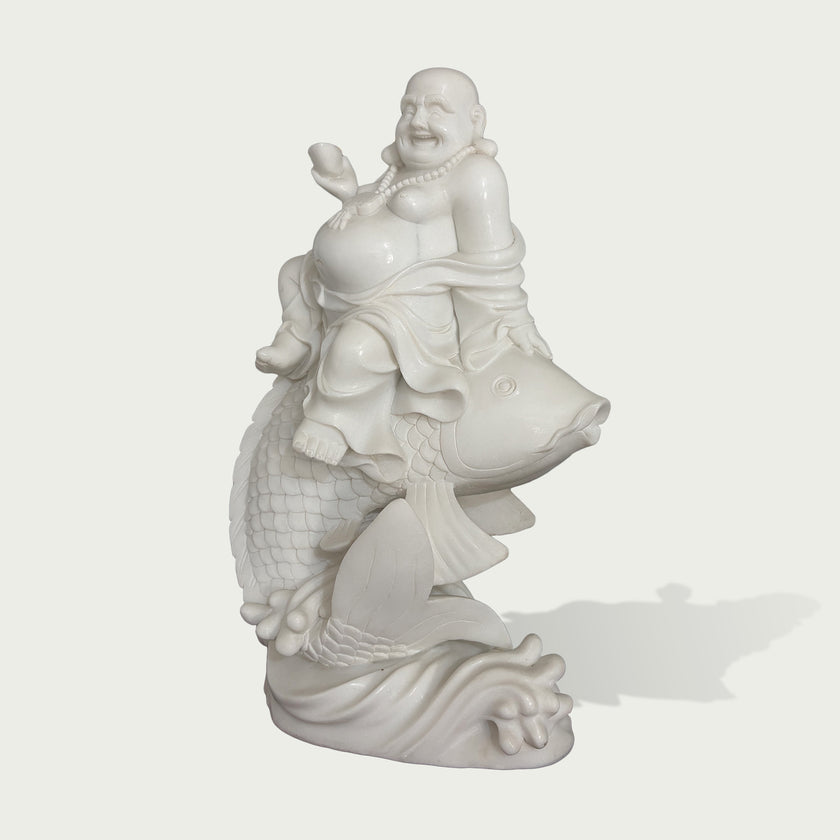Three-quarter view of a white marble Buddha riding a fish statue, showing intricate carving, joyful expression, and traditional symbolism of wealth and prosperity.