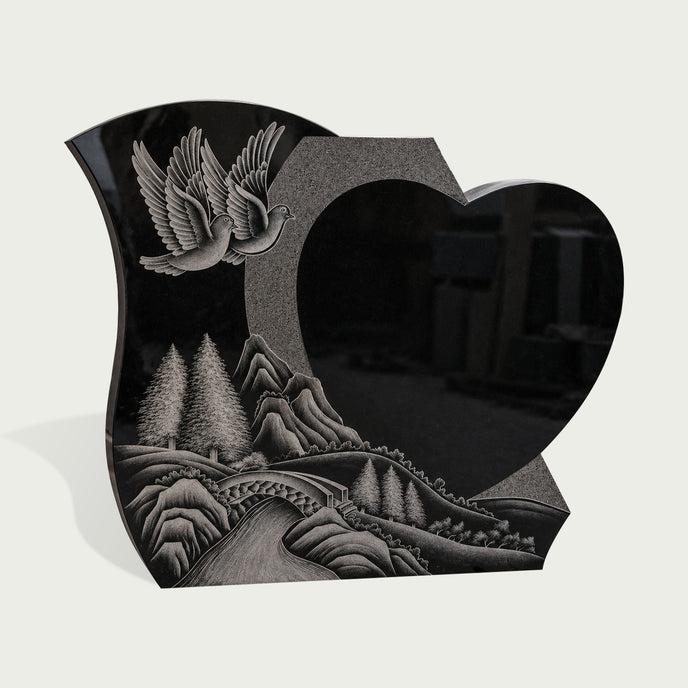 Polished black granite heart memorial marker featuring carved white doves, forest scenery, mountains, and river landscape design for a meaningful grave monument.