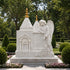 Elegant white marble angel grave marker with praying angel figure, church architecture, golden roof finials, floral carvings, and outdoor cemetery setting.
