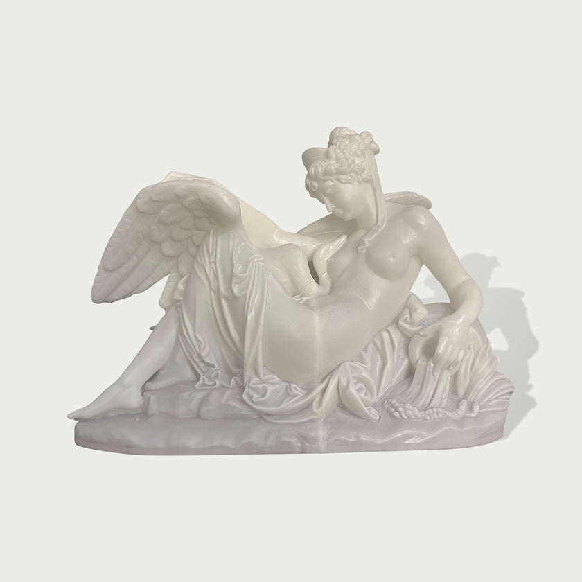 White marble sculpture of a reclining angel figure with large wings, flowing fabric, and classical carved details