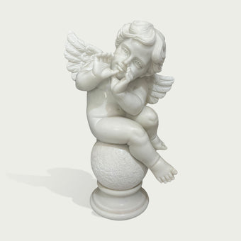 A white marble cherub figurine sitting on a round pedestal, with small wings and a thoughtful expression, photographed against a light gray background.