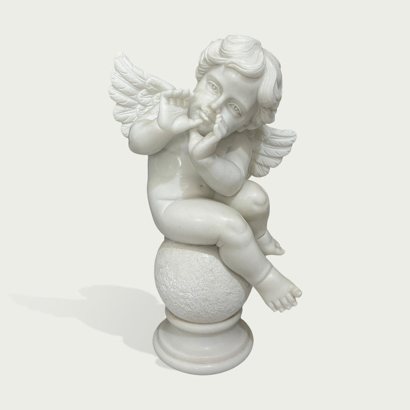 A white marble cherub figurine sitting on a round pedestal, with small wings and a thoughtful expression, photographed against a light gray background.