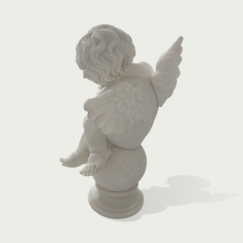 A white marble-style cherub statue shown from the back, seated on a round pedestal against a light gray background.