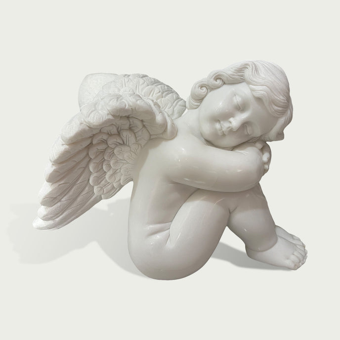 Close view of a white marble angel cherub sculpture with smooth carved details, feathered wings and tranquil sleeping design.