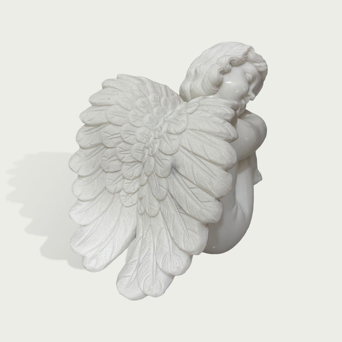 White marble cherub angel sculpture showing detailed feathered wings and peaceful sleeping pose with classical handcrafted stone carving.