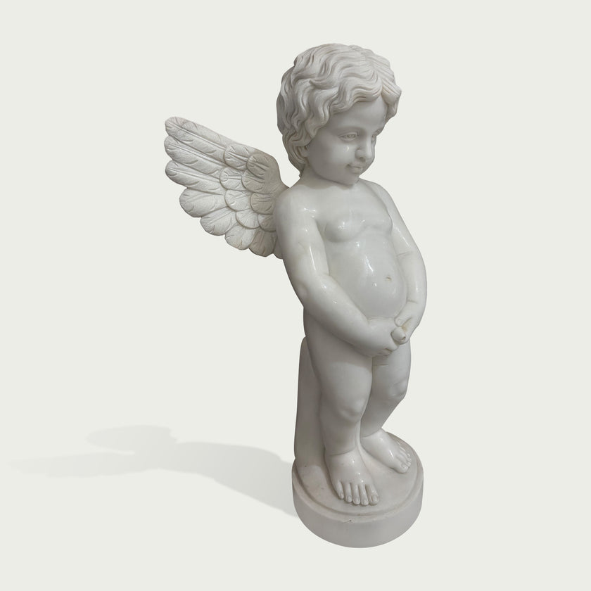 Side view of a white marble cherub angel statue showing detailed wing carving, curly hair, standing child figure, and elegant stone craftsmanship.