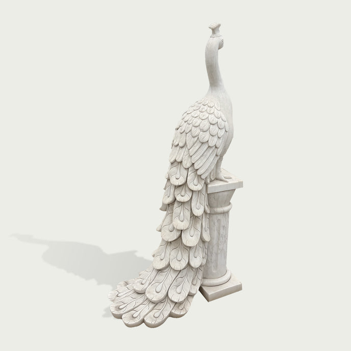 White marble peacock statue standing on a classical pedestal, featuring intricately carved layered feathers, elegant neck details, and long decorative tail.