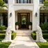 A symmetrical, luxurious white stucco house entrance with a stone pathway leading to double doors, flanked by manicured hedges, potted plants, and two large white peacock statues on pedestals.