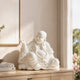 White marble Laughing Buddha statue placed on a modern cabinet, featuring peaceful expression, flowing robes, prayer beads, and spiritual home decor style.