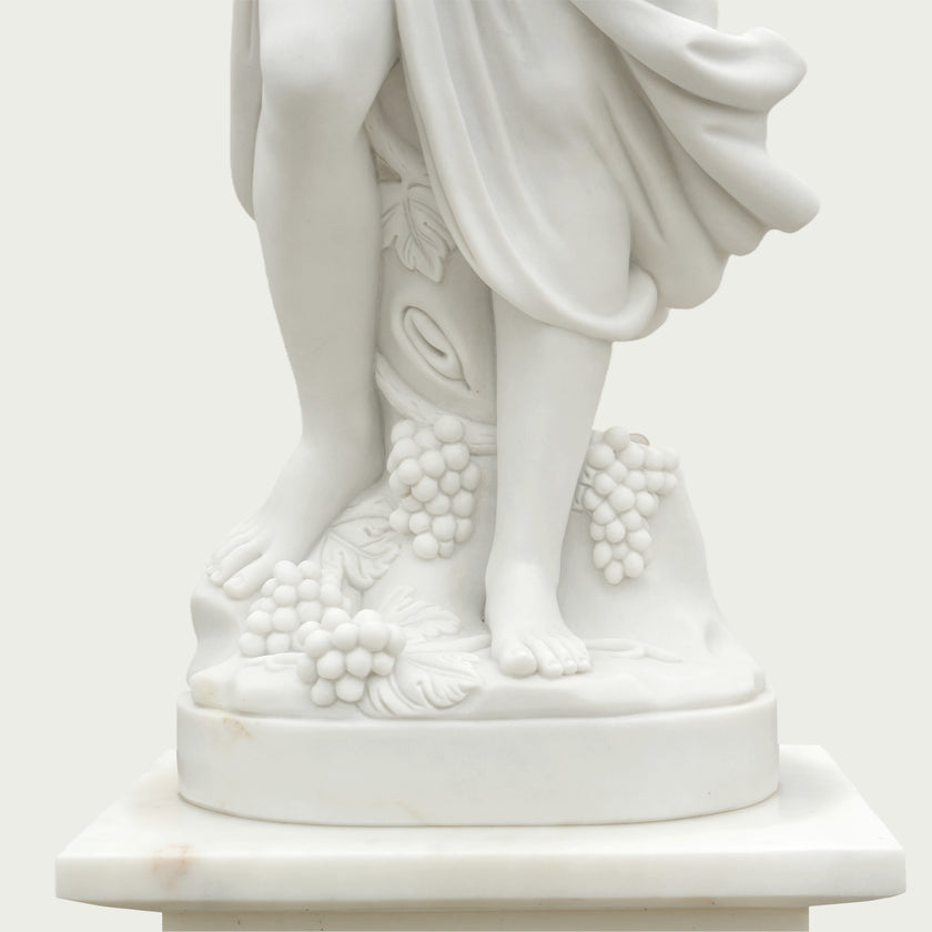 Close-up of the white marble violinist statue base showing finely carved bare feet, grape clusters, leaves and smooth polished marble craftsmanship.