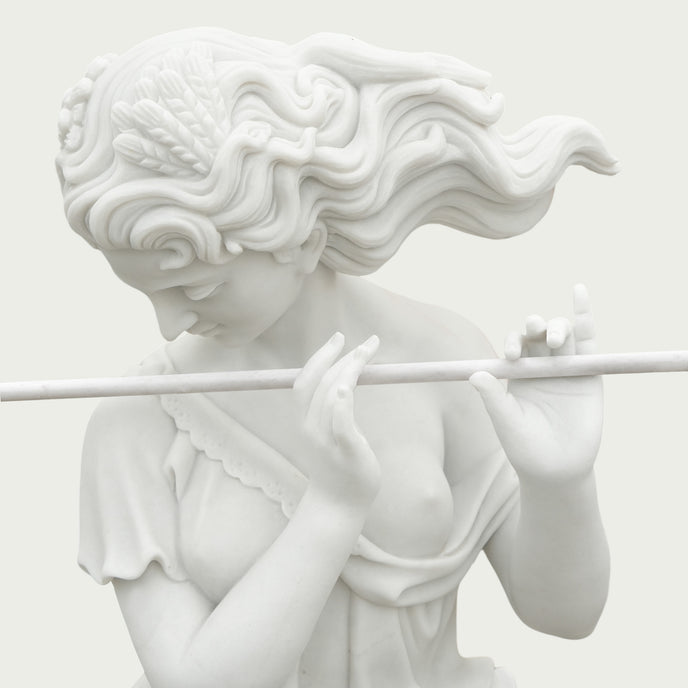 Close-up of a hand-carved white marble female flute player showing delicate facial features, flowing wavy hair, graceful hands and finely carved flute details.