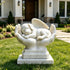 White marble sleeping angel dog memorial sculpture with detailed feathered wings, gently resting in two protective hands and displayed on a lawn outside a residential home.