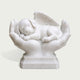 White marble pet memorial sculpture featuring a peaceful sleeping puppy with a detailed feathered angel wing, cradled in two caring hands on a carved pedestal base.
