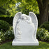 White marble sleeping angel memorial sculpture displayed in a peaceful garden, featuring detailed feathered wings, carved lilies, a blank inscription panel, and a solid marble base.