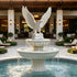 White marble eagle fountain installed in a luxury resort courtyard, featuring a detailed eagle with raised wings above two tiered basins, flowing water streams, a fluted classical pedestal, and a surrounding circular pool.