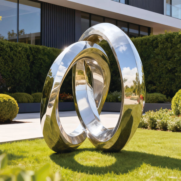 Modern stainless steel sculpture of two interlocking rings in a garden setting