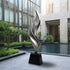 Abstract Stainless Steel sculpture in front of a modern building with a pool