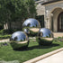 Three large stainless steel spheres on a grassy lawn in front of a house.