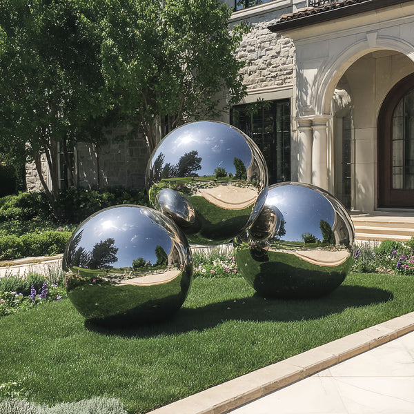 Three large stainless steel spheres on a grassy lawn in front of a house.