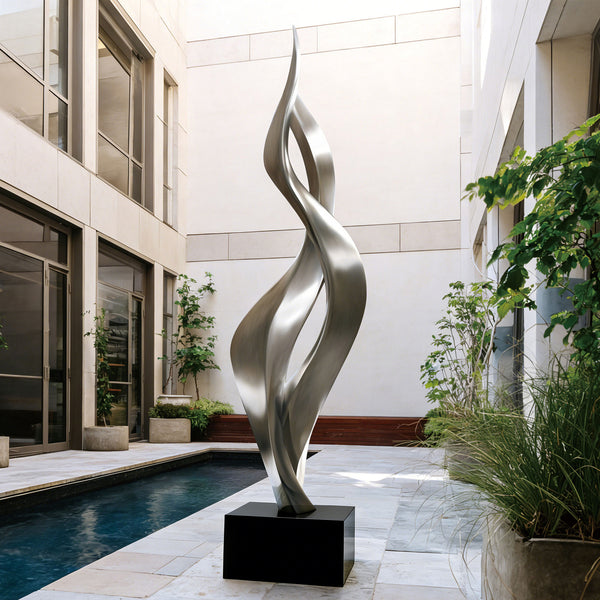 Modern tewsting silver stainless steel sculpture in a courtyard with architectural elements and plants