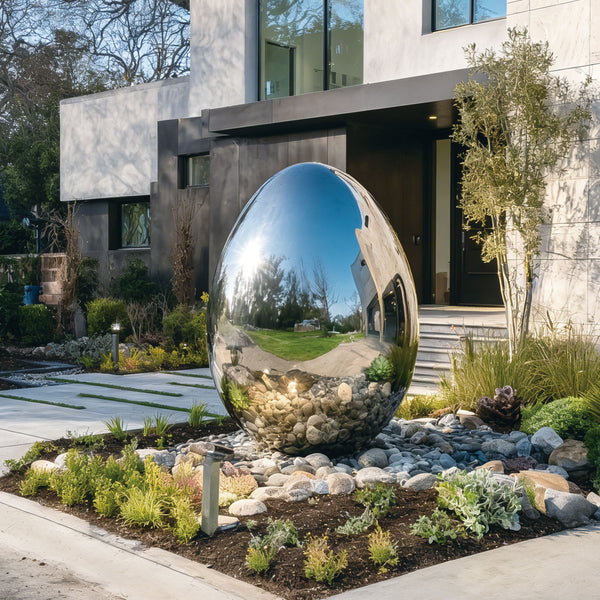Large stainless steel sphere egg shape in a garden setting with a modern building in the background