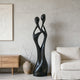 Black Abstract Intertwined Lovers Stainless Steel Sculpture in a minimalist living room setting with a beige sofa and wooden side table.
